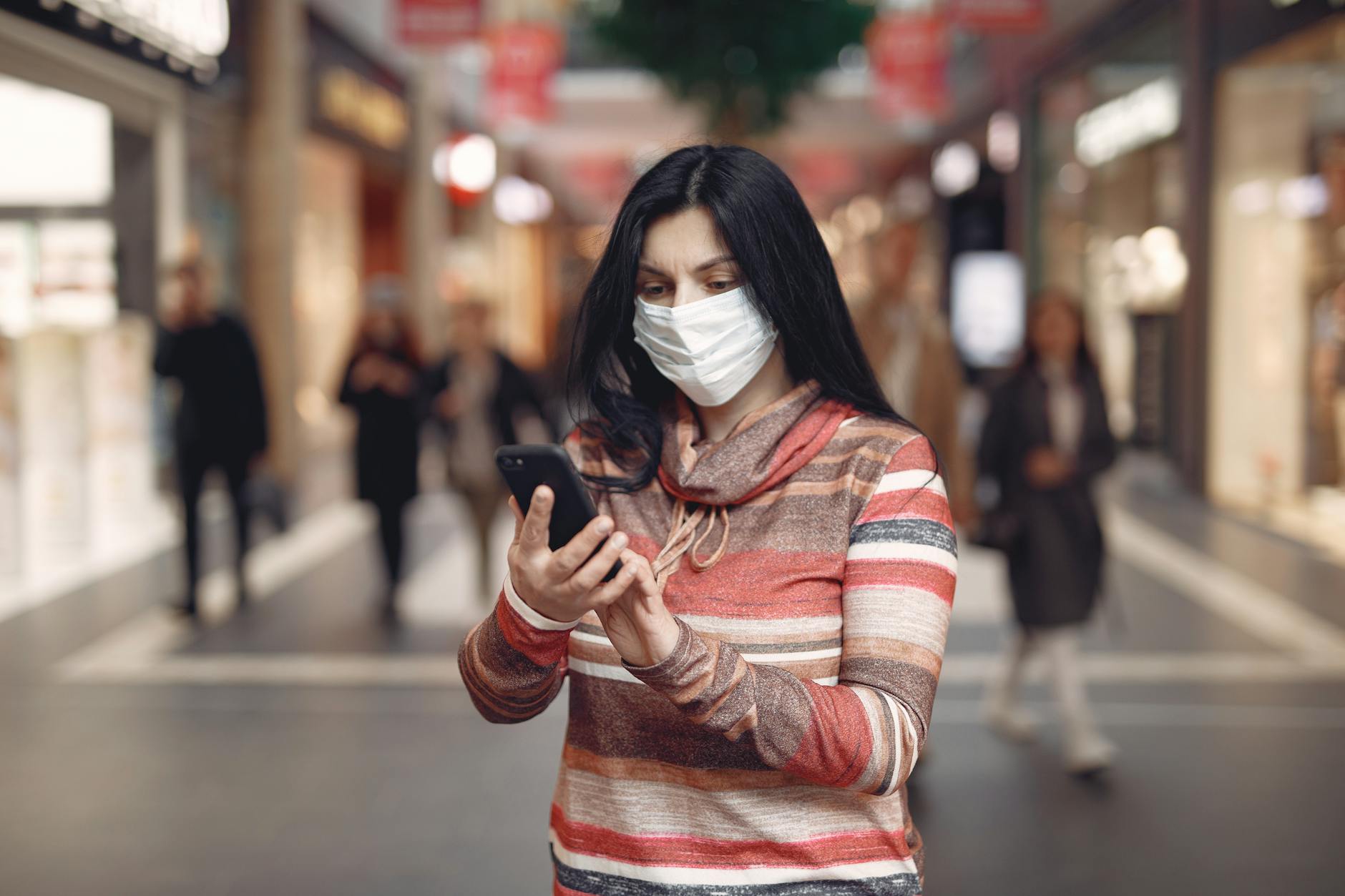 young woman wearing medical mask taking selfie in shopping center